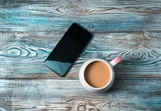 Mobiele telefoon en een kopje koffie op een houten tafel.