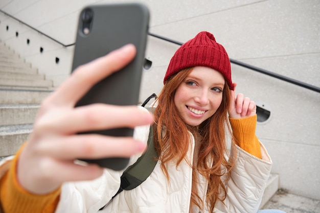 Foto mobiele telefoon en mensen lifestyle stijlvolle roodharige meid neemt selfie op haar smartphone poseert voor foto