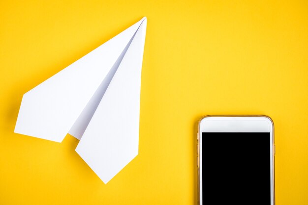Mobiele telefoon en papieren vliegtuigje op geel