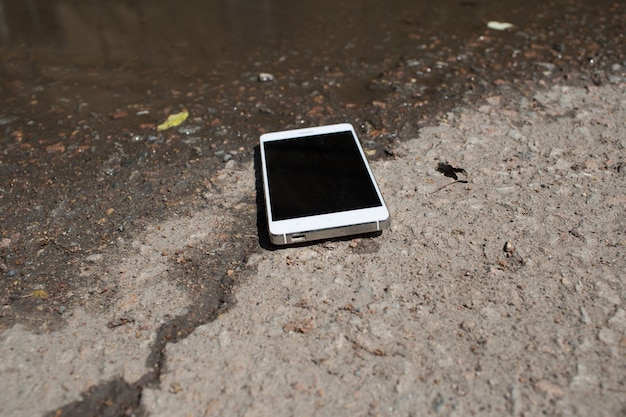 Mobiele telefoon liggend op de stoep in een plas.