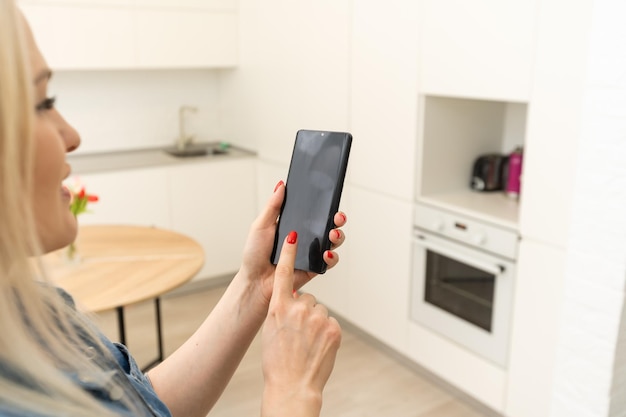 Mobiele telefoon met home control systeem op een scherm. slim huis, domotica, apparaat met app-pictogrammen. vrouw gebruikt haar smartphone met smarthome security app om de deur van haar huis te ontgrendelen.