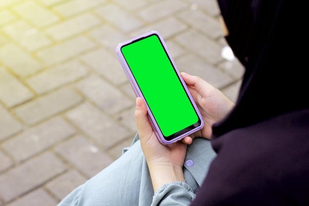 Mobiele telefoon mock-up met leeg groen scherm in vrouwelijke hand Aziatische moslim in tuin zomer.