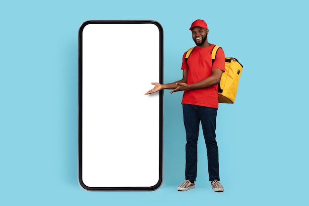 Mobile ad black delivery guy with thermal backpack pointing at blank smarthone