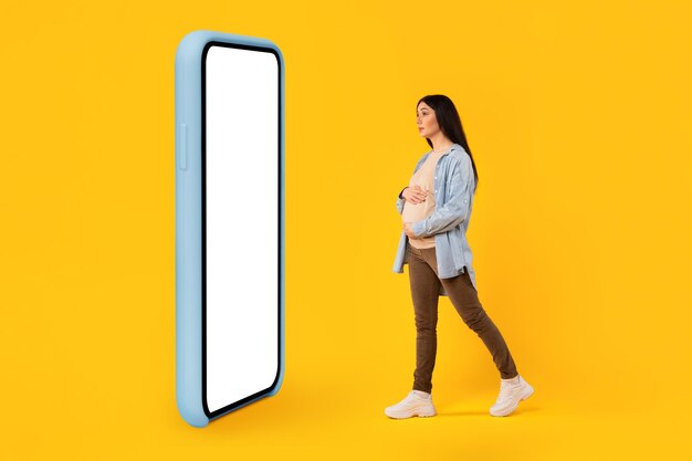 Photo mobile app for pregnancy pregnant lady standing in front of big cellphone with blank screen mockup