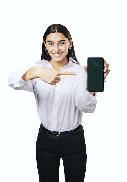 Mobile application concept with happy girl in white shirt showing modern smartphone with blank screen isolated on light background mockup