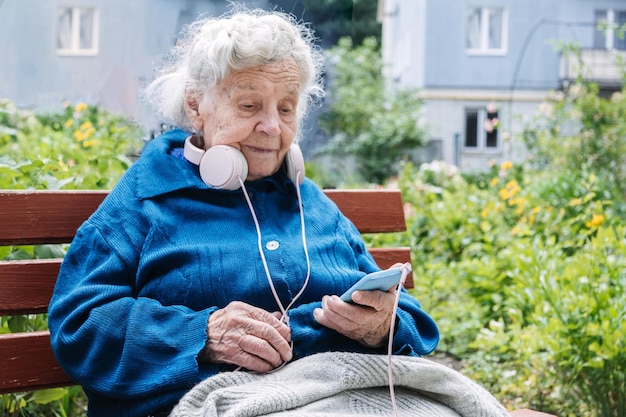 노인을 위한 모바일 앱 및 노인을 위한 노인 애플리케이션 야외에서 스마트폰 헤드셋을 사용하는 성숙한 노인 여성