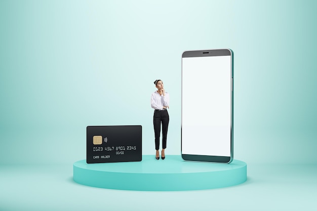 現代のスマートフォンの中で物思いにふける女性とのモバイルバンクと銀行のコンセプトで、ウェブデザインまたはアプリケーション用のスペースを備えた空白の白い画面と、明るい背景のモックアップのスタンドに黒いクレジットカードがあります