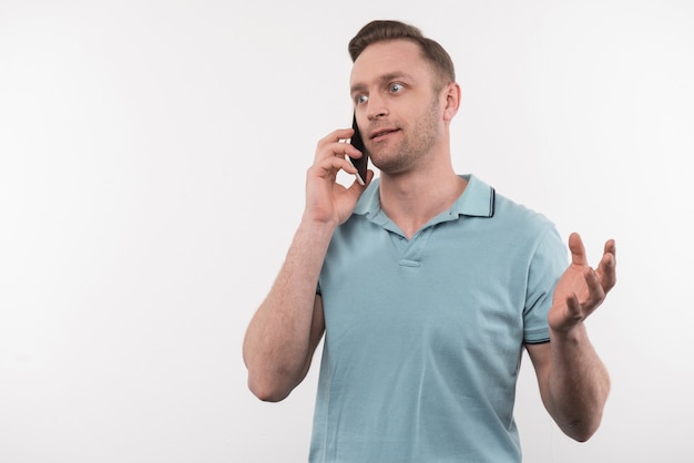 Mobile communication. Handsome emotional man talking on the phone while standing against white background