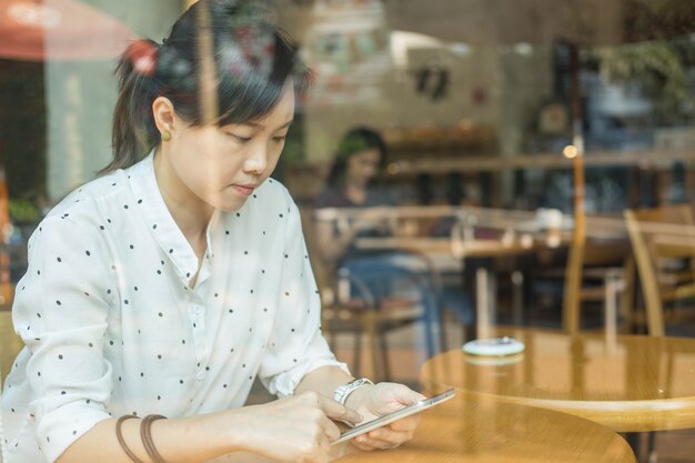 モバイルライフスタイル。アジアの女性はチャットや喫茶店で働くためにスマートフォンを使用しています。