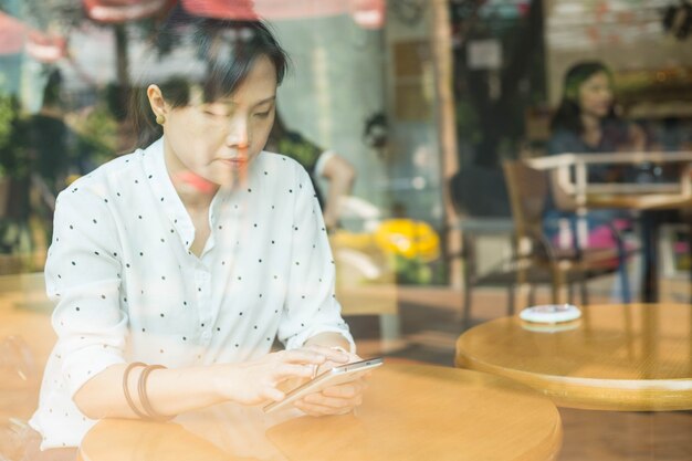 모바일 라이프 스타일. 아시아 여성은 스마트 폰을 사용하여 채팅하고 커피숍에서 일합니다.