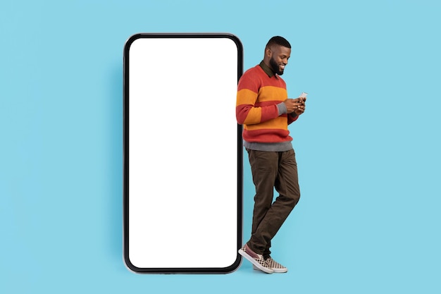 Мобильное предложение Улыбающийся пустой человек со смартфоном, стоящий возле большого пустого телефона