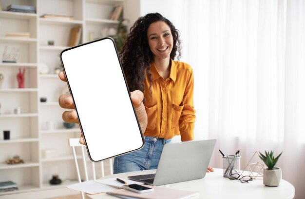 Mobile offer smiling female freelancer showing big blank smartphone at camera