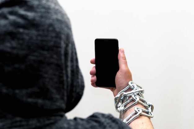 Foto telefono cellulare incatenato alle mani di un uomo con cappuccio telefono sfondo di studio bianco