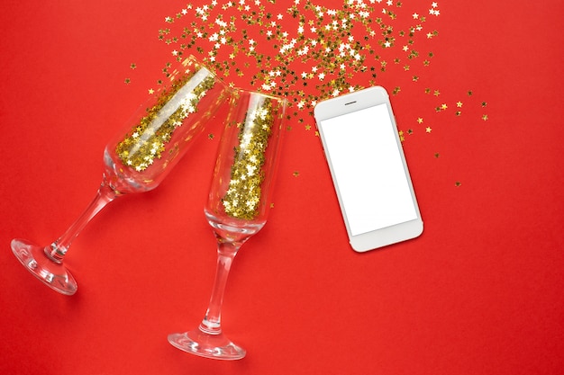 Mobile phone and champagne glasses with golden stars confetti, christmas and new year concept