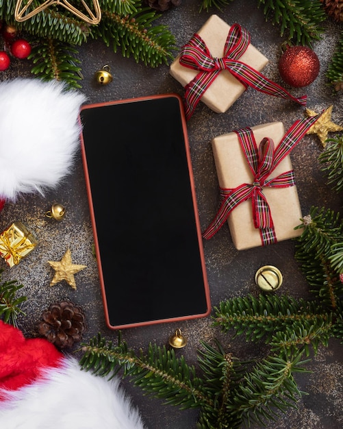 mobile phone between christmas decorations santa claus hat gift boxes and green fir branches