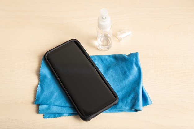 Mobile phone, cloth and alcohol spray bottle on table. Clean smartphone concept