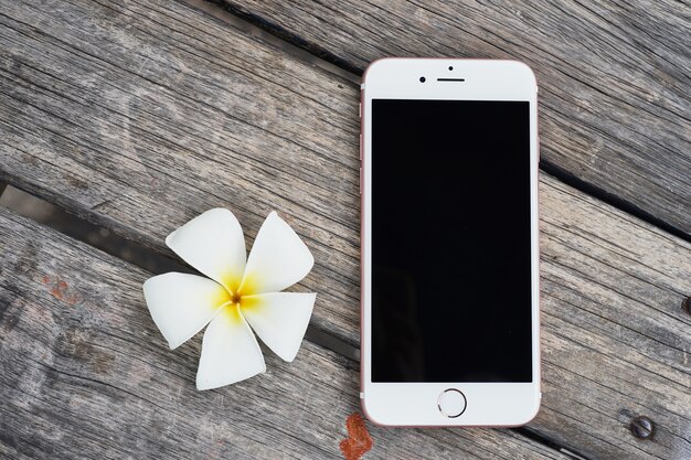 Foto telefono cellulare o dispositivo con il bello fiore su fondo di legno