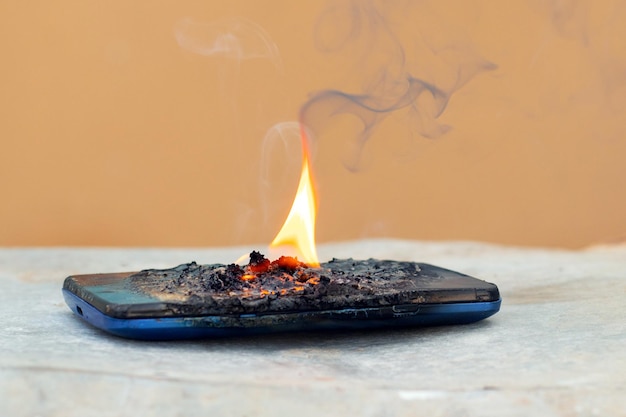 Мобильный телефон в огне и дыму Телефон загорелся из-за неосторожного обращения
