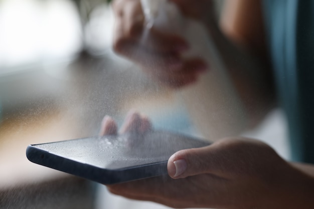 Mobile phone in hands of woman is treated with antiseptic spray