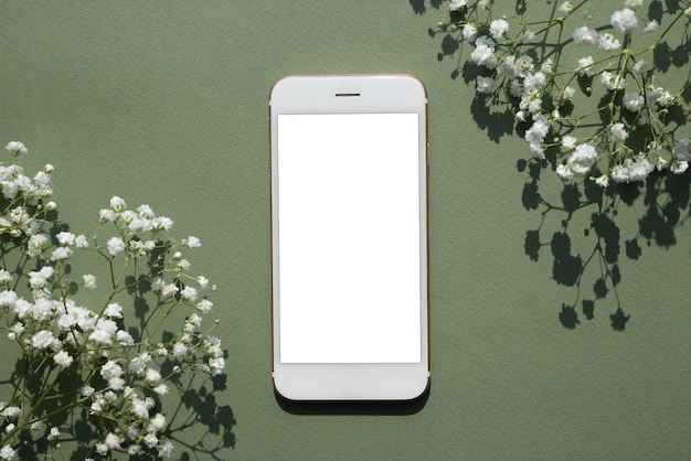 Photo mobile phone mock up on a pastel green background decorated with white small flowers top view