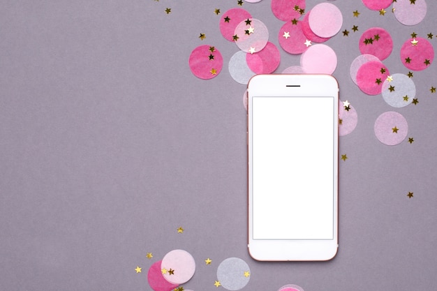 Mobile phone mock up and pink confetti with gold stars on gray  