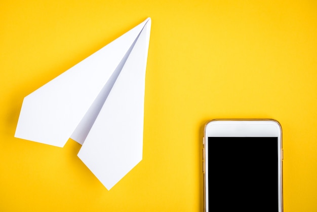 Telefono cellulare e aeroplano di carta su giallo