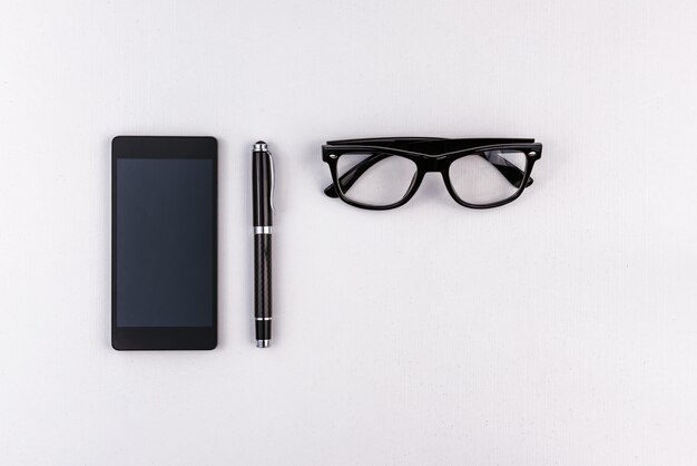 Mobile phone, pen and eyeglasses on white surface