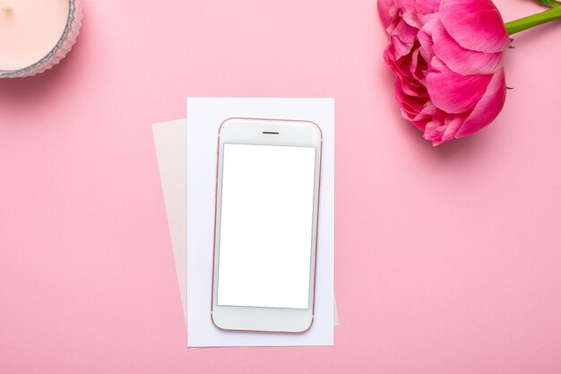Mobile phone and peony flower on pink pastel table in flat lay style. Female working desk. Summer colour