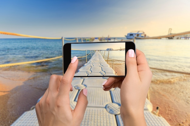 Mobile phone photography of a beach wide view horizontal. Close-up hand holding phone shooting beach