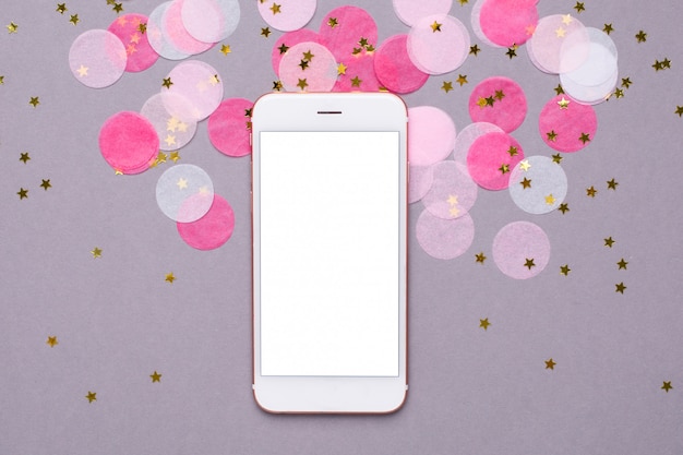 Mobile phone and pink confetti with gold stars on gray  