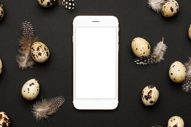 Mobile phone and quail eggs with feathers on a black background. Holiday easter, minimalistic black composition