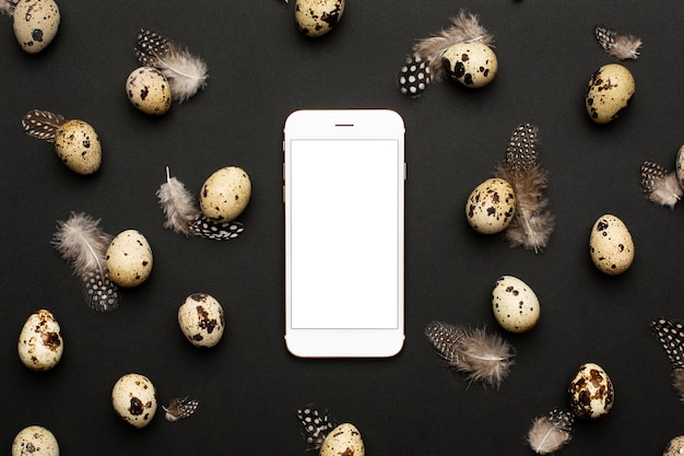 Mobile phone and quail eggs with feathers on a black background. Holiday easter, minimalistic black composition