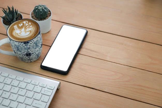 Foto schermo del telefono cellulare e caffè caldo del cappuccino di arte accanto alla tastiera senza fili su una tavola di legno