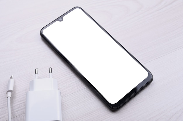 Mobile phone smartphone with white screen for your text, image on a bright defective table with charging