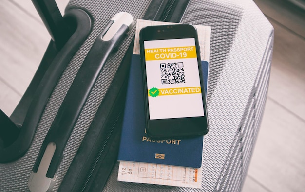 Mobile phone on the suitcase and health passport of vaccination\
certification on the screen