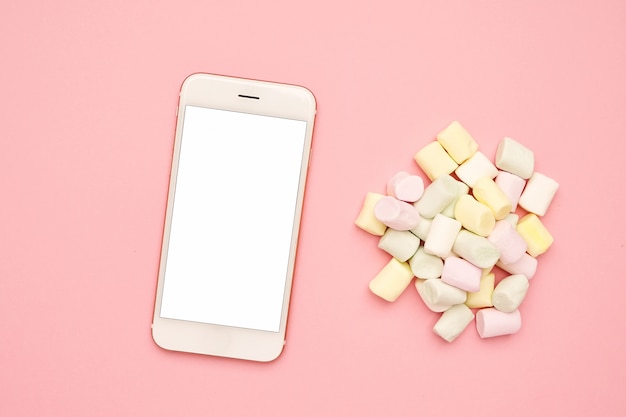 Mobile phone and sweet marshmallows on a pink 