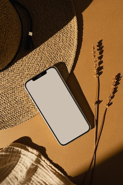 Фото Мобильный телефон с пустым экраном для копирования. соломенная шляпа, муслиновая ткань, сухая трава на оранжевом фоне с солнечными тенями. эстетическая минимальная модная композиция.