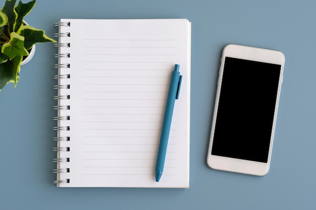 Mobile phone with blank on screen notebook paper and pen isolated on gray background