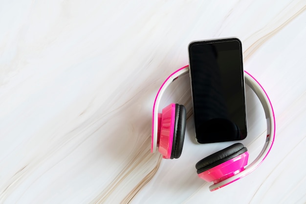 Mobile and pink headphone on white marble table with free copy space for text.