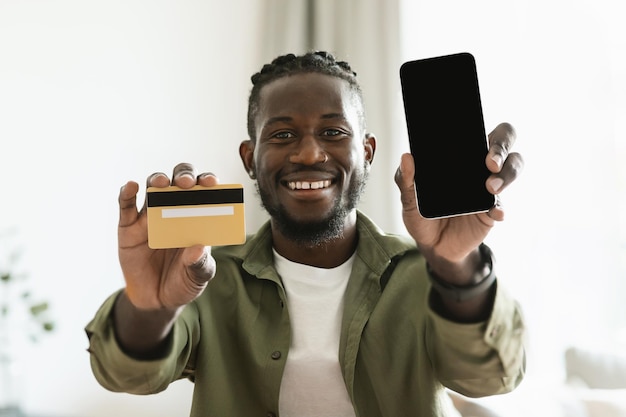 Mobile shopping appliation Happy black guy holding credit card and showing smartphone with blank screen mock up