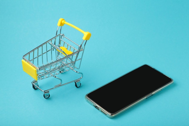 Concetto di applicazione per supermercati per lo shopping mobile smartphone e mini carrello su sfondo blu vista dall'alto