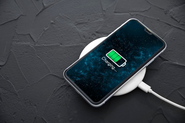 Foto smartphone mobile sul dispositivo di ricarica wireless su sfondo scuro. icona della batteria e illuminazione di avanzamento della carica sullo schermo. smartphone collegati alla fonte di alimentazione. problemi di livello di batteria basso. telefono collegato