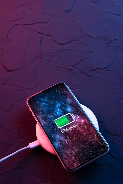 Smartphone mobile su dispositivo di ricarica wireless su sfondo di colore rosso e blu neon scuro. icona della batteria e illuminazione di avanzamento della carica sullo schermo. smartphone collegati alla fonte di alimentazione. batteria scarica