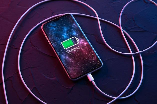 Photo mobile smart phone on wireless charging device on dark neon red and blue color background. icon battery and charging progress lighting on screen.smartphones connected to power source.low battery