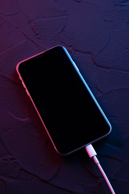 Mobile smart phone on wireless charging device on neon background. Icon battery and charging progress lighting on screen.smartphones connected to power source.low battery level problems.Plugged Phone.