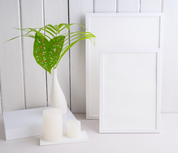 모의 uo 포스터 프레임과 야자수는 흰색 테이블 벽 배경에 있는 아름다운 흰색 세라믹 꽃병에 식물 열대 집 식물을 남깁니다.