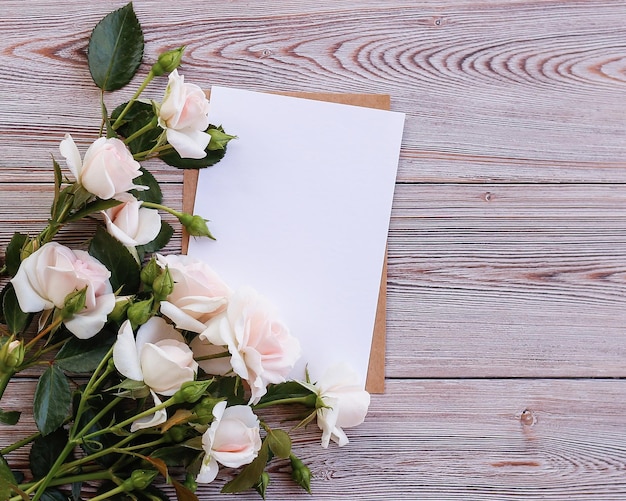 木製の背景に繊細なバラのテキストの空白の白い紙のカードをモックアップ