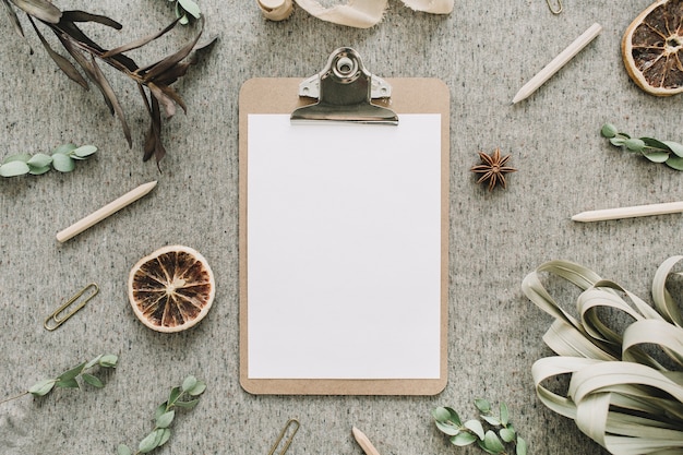 Mock up clipboard in frame of dry leaves and oranges, eucalyptus branches on beige rustic blanket background. Flat lay, top view