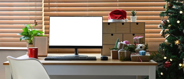 Mock-up computer met witte display, kamerplant en kerstcadeaus op houten tafel.