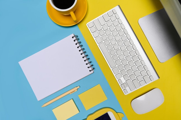 青と黄色の背景にコンピューター、メモ帳、コーヒーカップ、携帯電話のモックアップ。